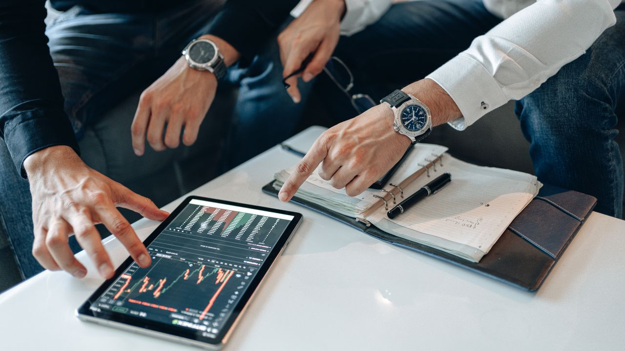 The Art of Drawing Readers In: Your attractive post title goes here Close-up of professionals discussing stock charts on a tablet with notes and pens on a table.